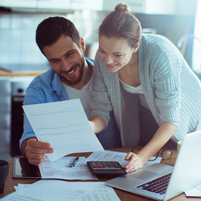 A young couple look through paperwork at their kitchen table.