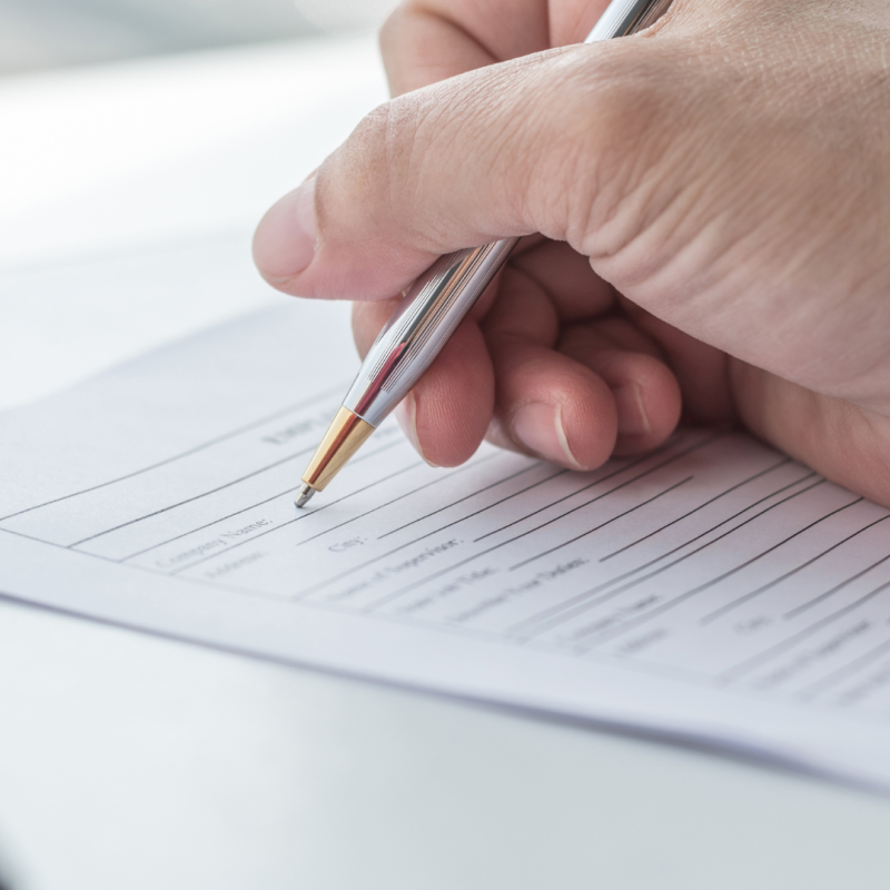Close up of a person's hand holding a pen, writing on a piece of paper.