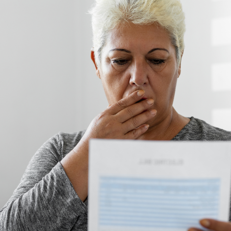 A woman covers her mouth in shock with one hand, the other is holding an energy bill in front of her.