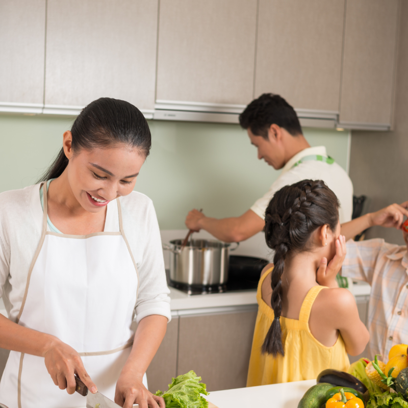A couple prepare dinner in a kitchen while their children play.
