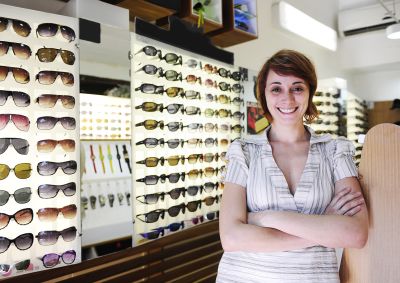 A female small business owner of an optometrist business standing in front of a glasses display.  