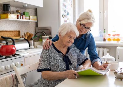 an elderly woman looking at her energy bill with another older woman looking over her shoulder