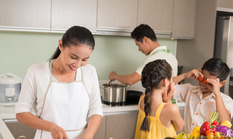 A couple prepare dinner in a kitchen while their children play.