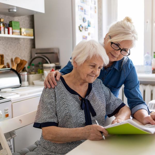 an elderly woman looking at her energy bill with another older woman looking over her shoulder